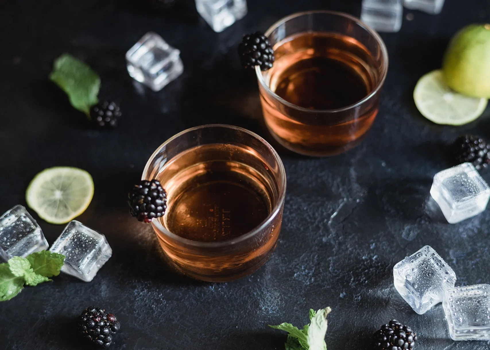 Vasos con cóctel, hielo, lima y moras