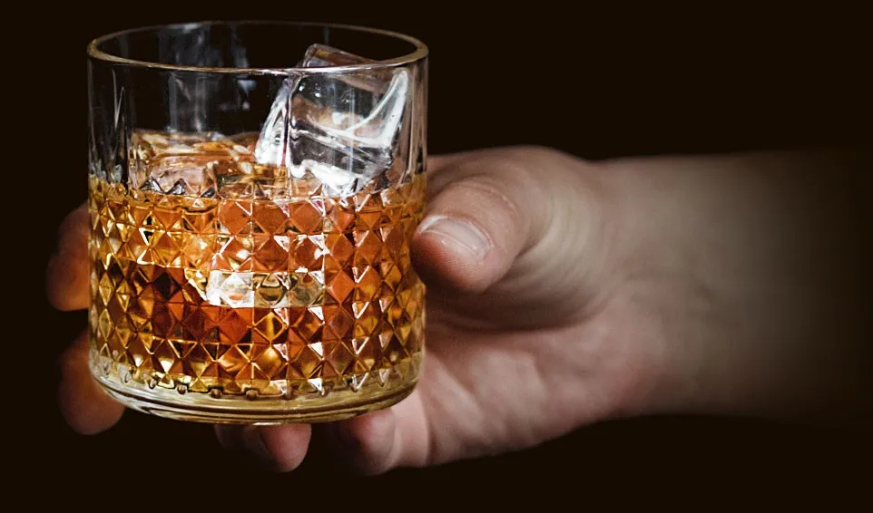 Mano sosteniendo un vaso de whisky con hielo